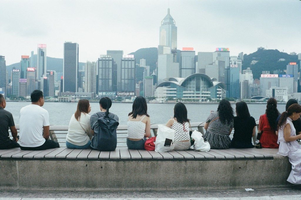 People sit on a wooden bench facing a city skyline